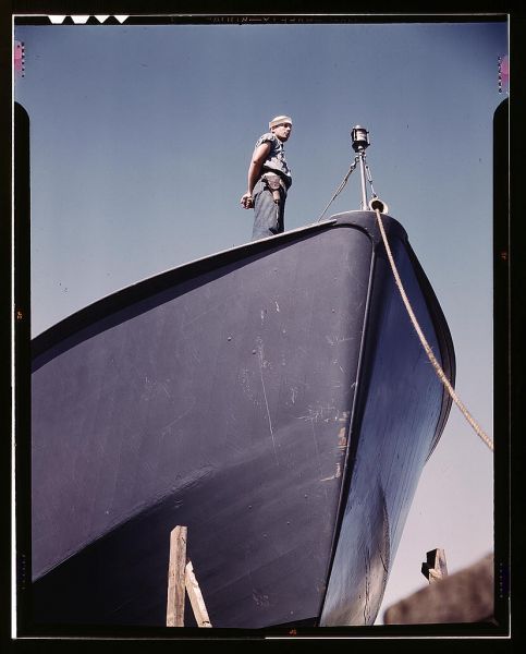 A Coast Guard sentry stands watch over a new torpedo boat under construction at a southern shipyard. In addition to wooden torpedo boats, the yard also turns out many steel boats for the Navy. Higgins Industries, Inc., New Orleans, La.  (LOC)